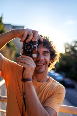 Sarı tişörtlü, elinde kamera olan yakışıklı, şık bir gencin portresi. film kamerası.