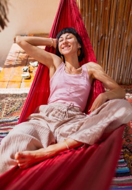 Tatilde hamakta dinlenen sakin bir genç kadın. Kız rahat bir şekilde dışarıda hamakta sallanıyor, stressiz bir hayat sürüyor. Yaz havası.