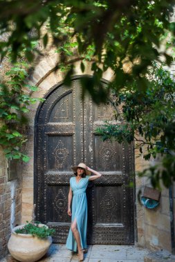 Neşeli gülümseyen stil sahibi bayan turist. Eski Jaffa şehrinde güzel caddelerde yürüyen elbiseli genç bir kadın. İsrail. Seyahat ve macera.