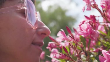 Güzel genç kız doğada pembe çiçeklerin kokusunu içine çekiyor, doğanın güzelliğini. Doğanın tadını.