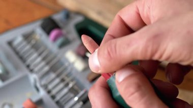 Bir adam ahşabı işledikten sonra bir elektrikli aletten bir eklentiyi çıkarır. Kum tahtası. Ellerin yakın çekimi.