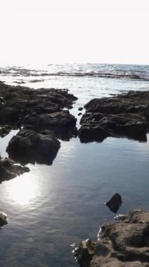 Dikey çekim. Deniz kıyısında taşların üzerinde zıplayan genç bir kadın. Kız deniz kenarında eğleniyor..