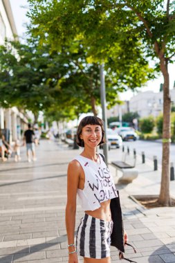 Kız güneşli şehir caddesinde yürüyor. Genç kız arkadaşlarıyla buluşacak. şehir tarzı, gülümseme, yaz trendi.