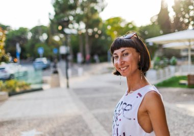 Güneşli şehir caddesinde yürüyen güzel esmer, şehir tarzı, gülümseme, yaz trendi.