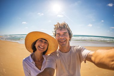 Mutlu bir çift yaz tatilinde sahilde selfie çeker. Genç turistler güneşli bir kaçamağın tadını çıkarıyorlar. Turizm, plaj, yaz ve seyahat kavramları.