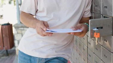Genç bir adam elinde zarflarla posta kutusunun önünde duruyor ve bir mektup okuyor. Posta alıcısı. Adam sokakta durur ve tutar.