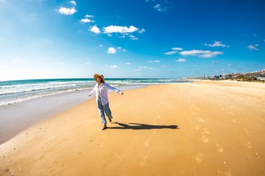 Kumsalda gülümseyen mutlu bir kadın. Güzel genç bir kadın boş bir sahil boyunca yürüyor. Mutlu bir kız yaz tatilinde beyaz kumlu bir plajda gezinir. Romantik ruh hali.