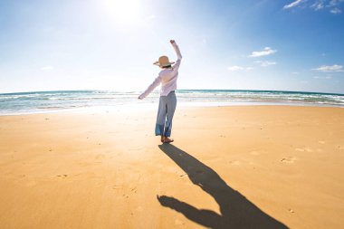 Mutlu, güzel genç bir kadın kumsalda geziniyor. Kaygısız bir kız güneşli bir günde sahilde gezinir. Plajda beyaz gömlekli ince bir kız..