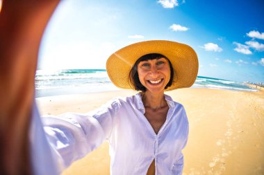 Sahilde selfie çekip kameraya bakan güzel bir kızın portresi. Kaygısız bir esmer yazın tadını çıkarıyor. Romantik bir ruh hali. Yaz yaşam tarzı.