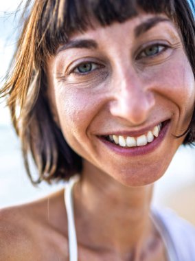 Gülümseyen bir kız sahilde dinlenir. Güzel bir kadın saçlarının rüzgarda savrulmasından hoşlanır. Çekici genç bir kadın yaz plajında temiz hava soluyor. Dinlenme ve rahatlama.