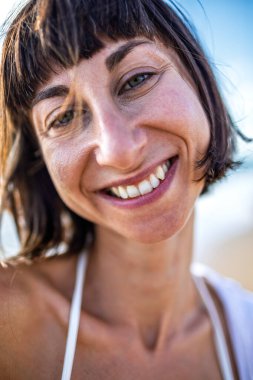 Gülümseyen bir kız sahilde dinlenir. Güzel bir kadın saçlarının rüzgarda savrulmasından hoşlanır. Çekici genç bir kadın yaz plajında temiz hava soluyor. Dinlenme ve rahatlama.