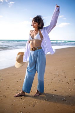 Gülümseyen bir kız sahilde dinlenir. Güzel bir kadın deniz kenarında bir andan zevk alır. Romantik bir ruh hali. Çekici genç bir kadın yaz plajında temiz hava soluyor. Dinlenme ve rahatlama.