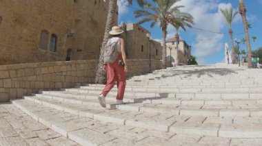 Sırt çantası ve kamerası olan bir bayan gezgin, ortaçağ şehrinde parlak yaz güneşinin altında yürüyor. Seyahat