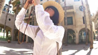 Tarz sahibi genç bir kadın sokakta yürüyor ve kamerayla fotoğraf çekiyor. Şık giyinmiş esmer bir kadın fotoğraf makinesiyle poz veriyor.