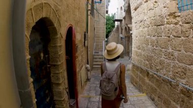 Sırt çantalı bir kadın turist şehrin eski turistik bölgesinde boş bir caddede yürüyor ve Jaffa 'daki tatilinin tadını çıkarıyor.