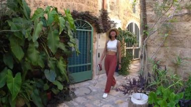 Kameralı bir kadın turist, şehrin eski turistik bölgesinde dar bir sokakta yürüyor ve Jaffa 'daki tatilinin tadını çıkarıyor.