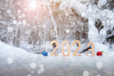 2023 ahşap yeni yıl rakamları, kış ormanlarındaki kar yığınlarında Noel topları, kar taneleri ve güneş ışınlarıyla birlikte. Yüzeyin derinliği. Mutlu yıllar 2023. Boşluğu kopyala