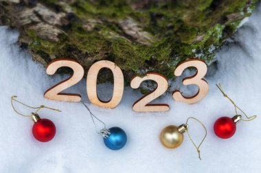 Yeni yıl 2023 ahşap parmaklar kar üzerinde duruyor. Soğuk kış günlerinde ağaçların gövdesine yaslanmış Noel topları ve açık havada yeşil yosunlar.