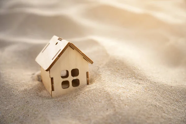 Small toy house in a deep sand with sand dunes nand sun rays. Real estate, natural disasters and cataclysms, sandstorms. Copy space