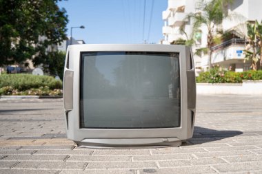 Güneşli bir yaz gününde şehrin asfaltında duran eski gümüş renkli TV seti.