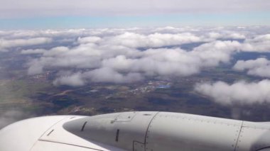 Bulut seviyesinde uçan bir uçağın penceresinden hava görüntüsü. Dünya görünür durumda. Uçak inmeden önce inmeye başladı. Gerçek zamanlı 4K videosu.