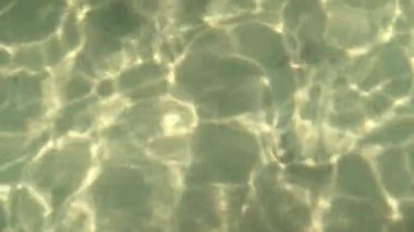 Ölü Deniz 'in dalgalanan berrak su yüzeyine sahip arka plan güneşli bir günde parlayan güneş ve altında tuz. 4K çözünürlük gerçek zamanlı video.