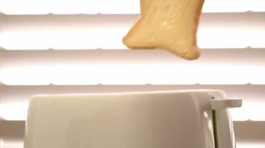 El, tost makinesine iki parça beyaz ekmek koyar ve arka planda parlayan ışıkla birlikte fırlarlar.