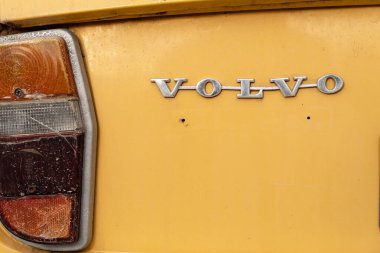 Rishon Lezion, İsrail - 15 Mayıs 2025. Eski Volvo metalik amblem rozeti turuncu bir arabanın arkasında kırık bir arabanın arka lambası var.