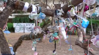 Dışarıdaki bir ağaç dalına asılı düzinelerce bebek emziği gösteren kamera çocukluk dönüm noktasını ya da ayini simgeliyor. 4K video