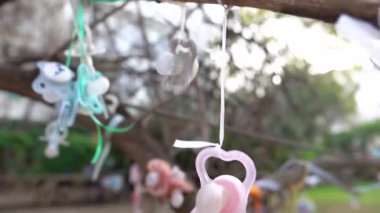 Dışarıdaki bir ağaç dalına asılı düzinelerce bebek emziği gösteren kamera çocukluk dönüm noktasını ya da ayini simgeliyor. 4K video