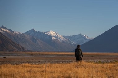 Genç adam güzel vadide duruyor. Arkasında dağlar ve sarı çayırlar var.