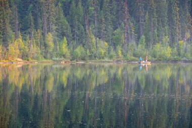 Güzel, sakin bir gölde küçük bir teknede balık tutan iki adam.
