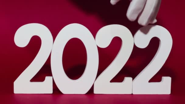 2022の数が赤の背景に白い木製の数字で表示され いくつかの手が白い手袋で最後の2を3に置き換え その結果 新年の数2023 — ストック動画