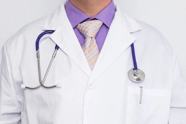 Stock image Close-up of chest of an unrecognizable caucasian doctor wearing a white coat over a purple shirt and necktie. A stethoscope hangs from his neck and pen is in the pocket.