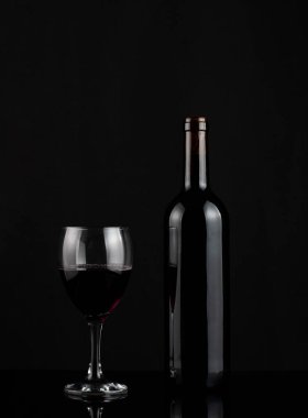 Siyah bir yansıtıcı yüzeyin üzerinde, bir şişenin yanında bir kadeh kırmızı şarap..