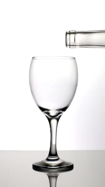 反射面の上に白ワイングラスを充填し 背景と認識できない人の垂直ビデオ — ストック動画