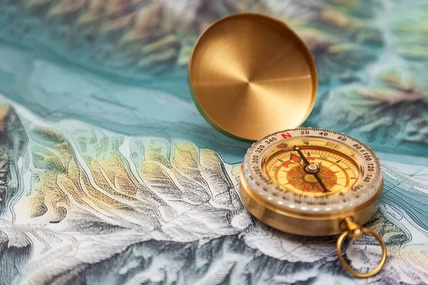 Close-up of a vintage gold compass on a map. Focus is centered on the compass north indicator, the rest is out of focus.