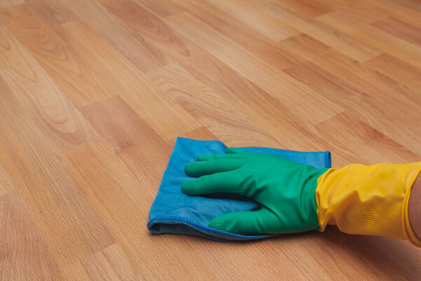 The hand of unrecognizable person wearing a rubber glove cleaning wooden parquet floor with a blue microfiber cloth.