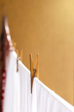 Çamaşır renginde bulanık giysiler, çamaşır ipinde asılı beyazlar, güneş ışığında kuruyup kahverengi duvara tahta mandallarla tutturulmuş.