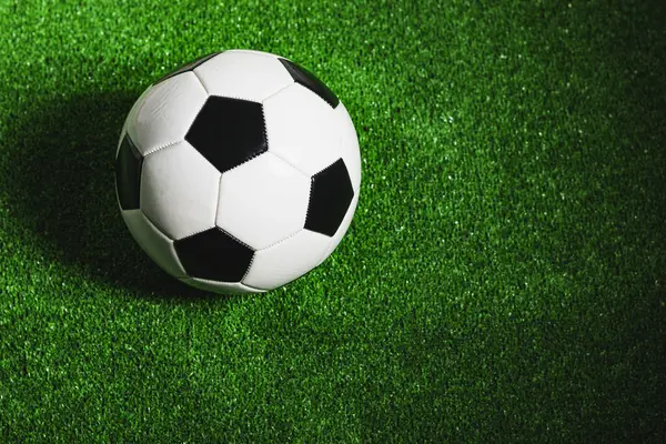A classic black and white soccer ball isolated on green grass seen from above.