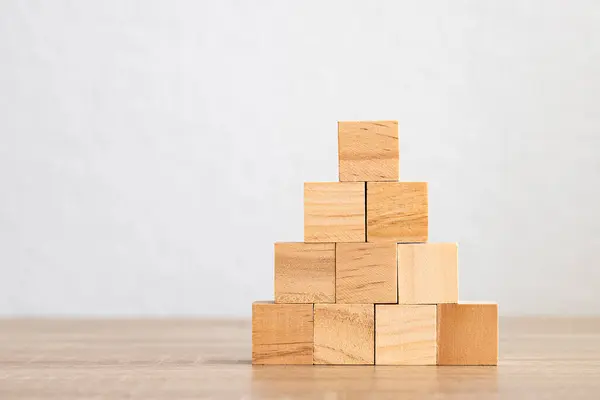 A neatly stacked pyramid of wooden blocks on a plain background.