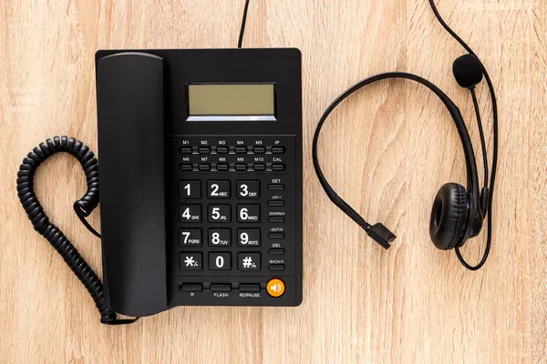 Çağrı merkezinin ahşap masasının üzerinde kulaklık takılı siyah bir telefon.