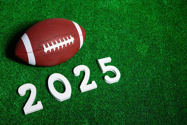 2025 'in yanındaki Amerikan futbol topunun figürleri yukarıdan görünen yeşil çimlerin üzerinde beyaz boyalı ahşaptan yapılmıştır..