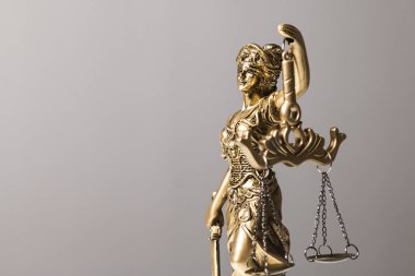 Adalet Tanrıçası 'nın altın bir heykelinin dörtte üçü, gözleri bağlı gri arka planda bir tartı tutuyor.