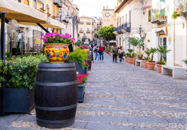 CEFALU, İtalya - 7 Nisan 2023: Sicilya adasındaki ortaçağ köyü Cefalu 'daki canlı cadde. Kafeler, tarihi binalar ve geleneksel Sicilya dekorasyonlu saksı ile turistik ilgi..