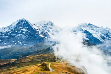 İsviçre Alplerinde sonbahar. İsviçre, Wengen ve Lauterbrunnen yakınlarındaki Mannlichen 'de yürüyüş yolunda. Eiger, Monch, Jungfraujoch ve Jungfrau zirveleri alçak bulutlarda..