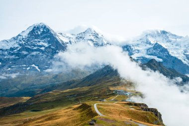 İsviçre Alplerinde sonbahar. İsviçre, Wengen ve Lauterbrunnen yakınlarındaki Mannlichen 'de yürüyüş yolunda. Eiger, Monch, Jungfraujoch ve Jungfrau zirveleri alçak bulutlarda..