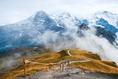İsviçre Alplerinde sonbahar. İsviçre, Wengen ve Lauterbrunnen yakınlarındaki Mannlichen 'de yürüyüş yolunda. Eiger, Monch, Jungfraujoch ve Jungfrau zirveleri alçak bulutlarda..