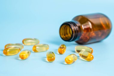 Omega 3 kapsülleri mavi arka planda, açık şişenin yanında. Balık yağı vitaminleri ve terapi ya da bilimsel araştırma malzemeleri. Yaklaş, seçici odaklanma.