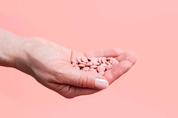 Close-up of many pink pills in woman hand on pink background. Medical concept of medicine treatment, vitamins, supplements, contraceptive pills or feminine drug addiction. Selective focus.